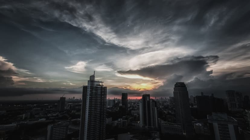 City skyscrapers stand beneath swirling dark clouds and golden sunset light during a dramatic storm.