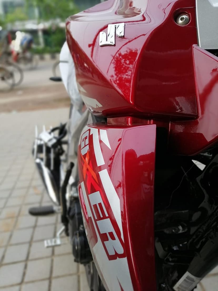 Red Suzuki Gixxer motorcycle fairing featuring white decals and a chrome exhaust in a blurred urban setting.