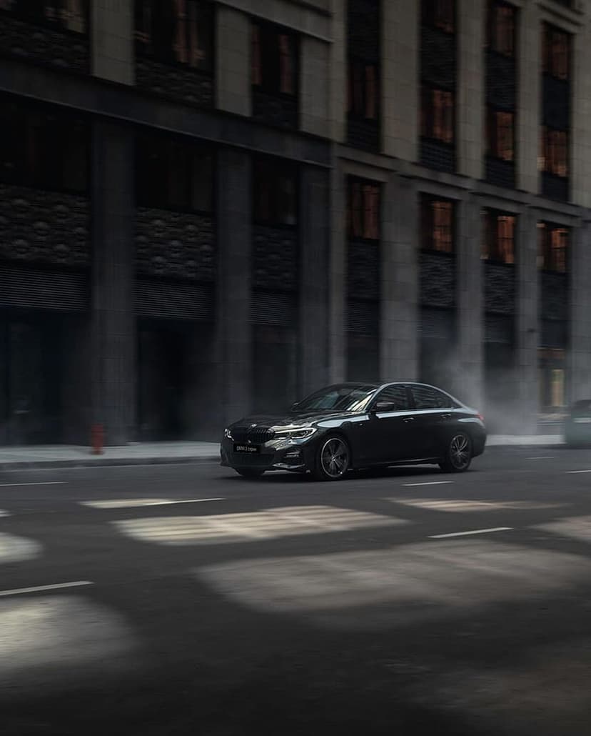 Black luxury sedan driving fast on a dark city street with motion blur and dramatic lights against stone walls.