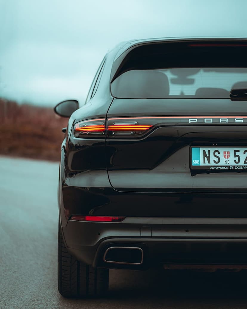 Porsche Cayenne SUV rear view featuring glowing red LED taillights and a chrome badge on a wet road surface.