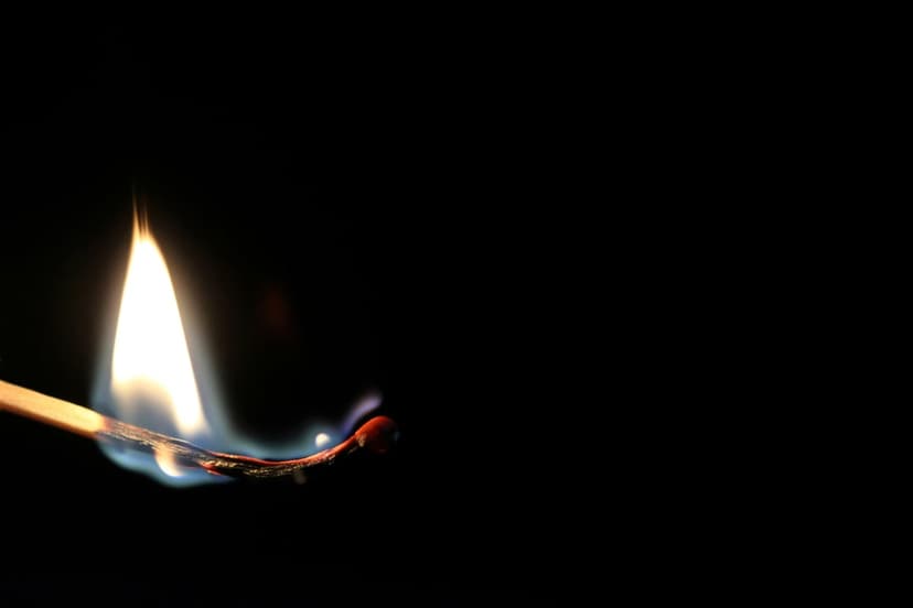 Ignited wooden matchstick producing a bright orange and yellow flame with blue accents against a black backdrop.