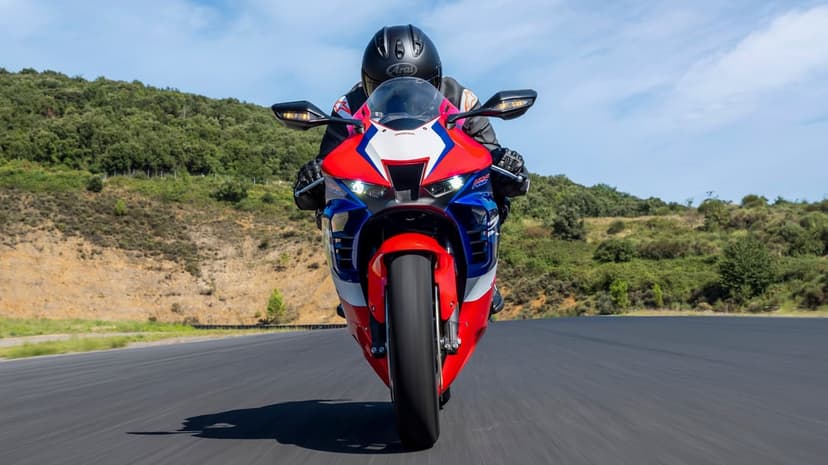 Motorcyclist on a red, white, and blue sportbike riding on a racetrack against a background of green hills.