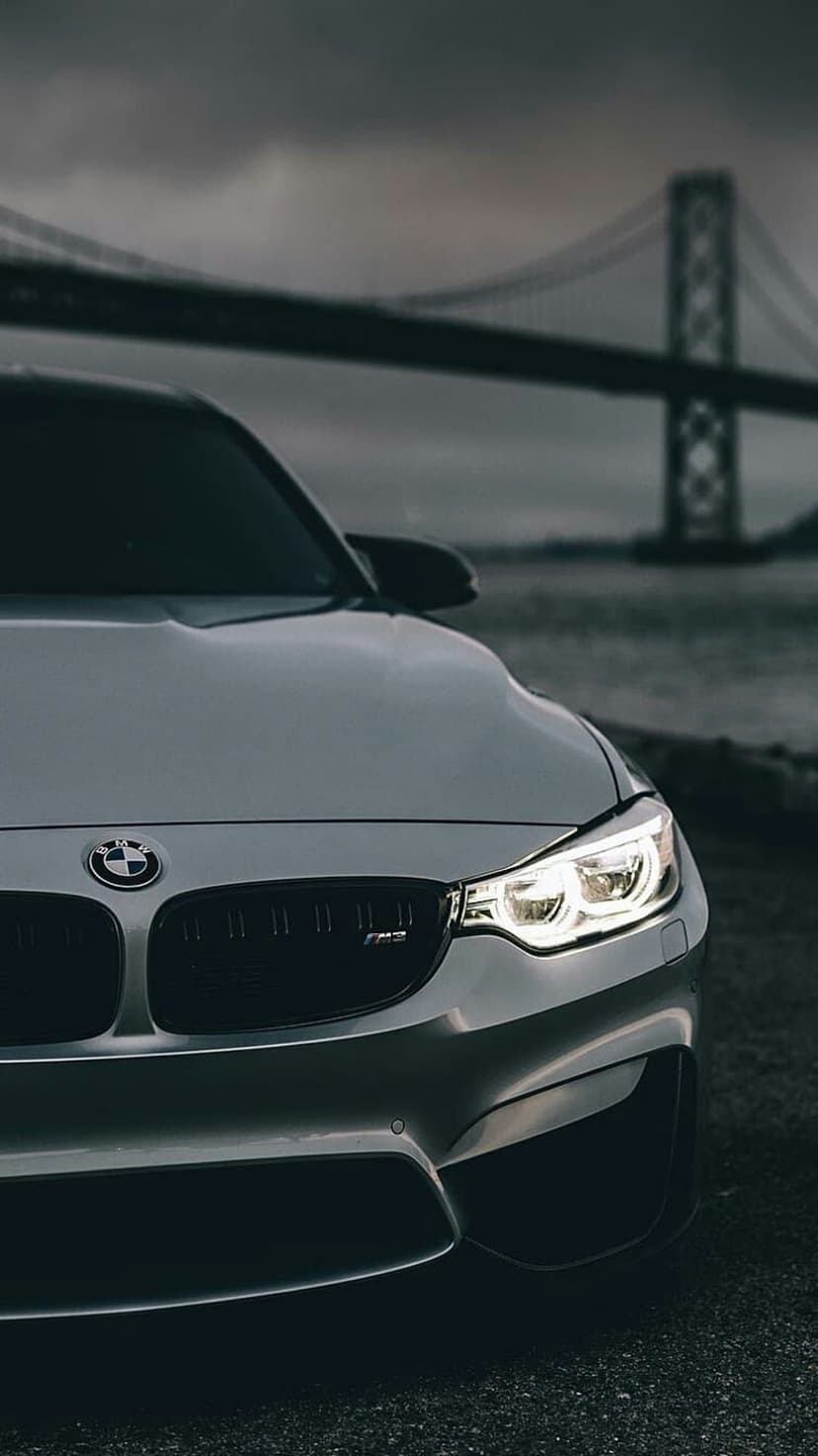 BMW M4 front grille and glowing headlights set against a hazy bridge and river during a moody twilight scene.