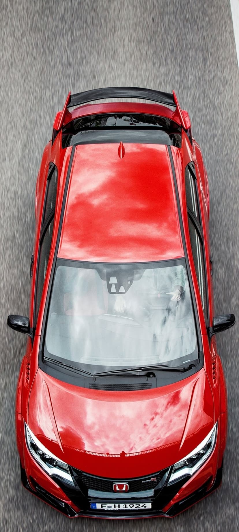 Red Honda Civic Type R with a large rear wing drives on a dark asphalt road, captured from directly above.