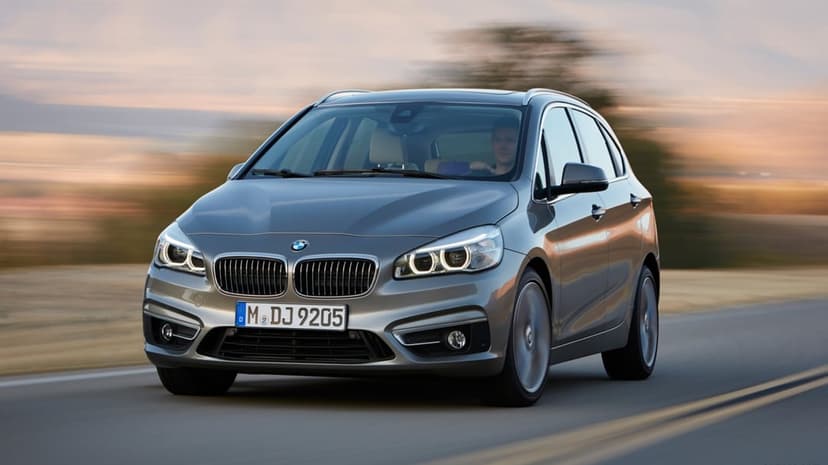 Silver BMW 2 Series Active Tourer driving on an asphalt road at sunset with motion blur and golden lighting.