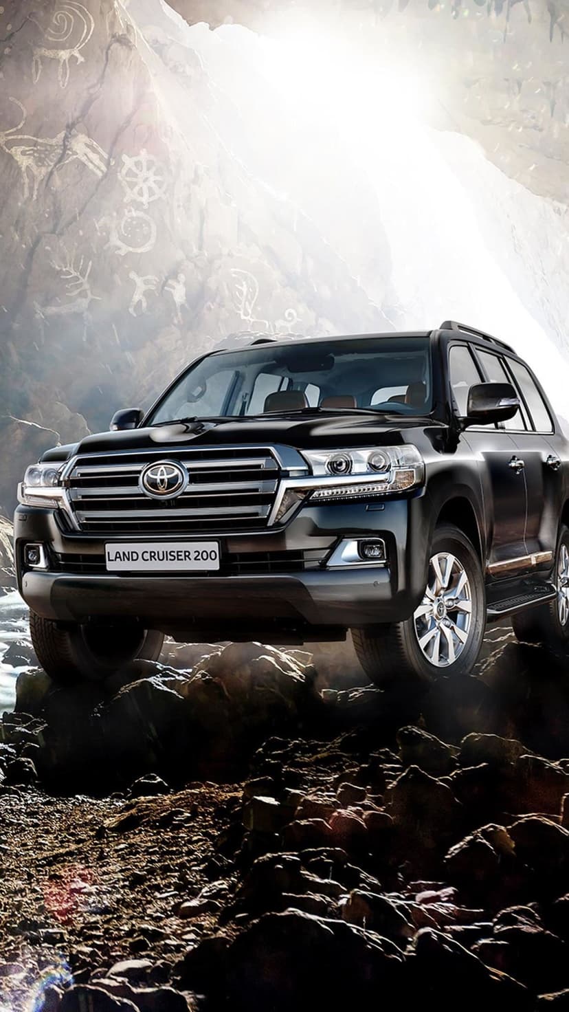 Black Toyota Land Cruiser 200 on rocky terrain with ancient petroglyphs and bright sunlight in a cavern.