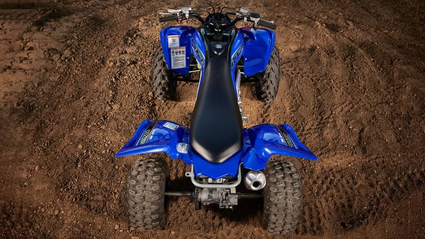 Top-down view of a blue Yamaha sport ATV on brown dirt with knobby tires and a black textured seat.