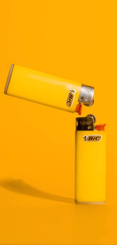 Two Yellow Bic Lighters on an Orange Background