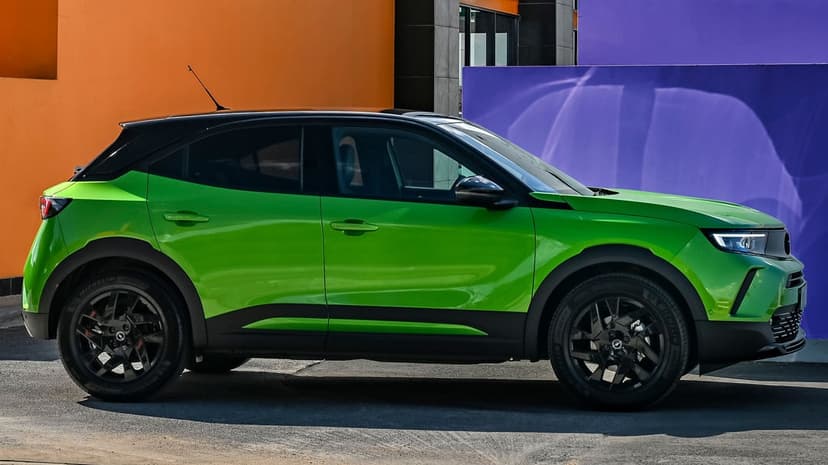 Side profile of a lime green Opel Mokka SUV between orange and purple walls on a sunny asphalt road.
