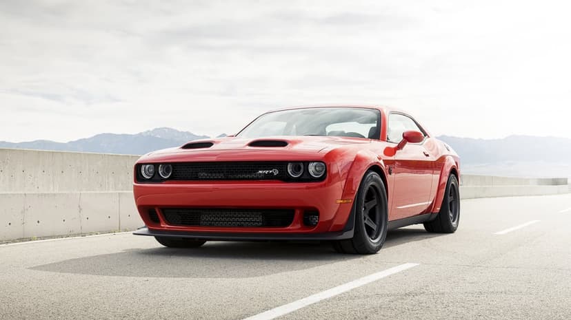 Red Dodge Challenger SRT Widebody muscle car parked on a paved road with distant mountains under a bright sky.
