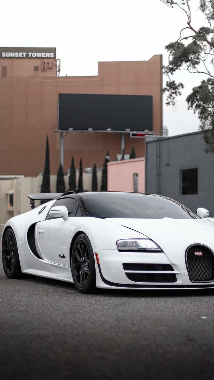 White Bugatti Veyron supercar sits on an urban street with the Sunset Towers sign visible in the background.