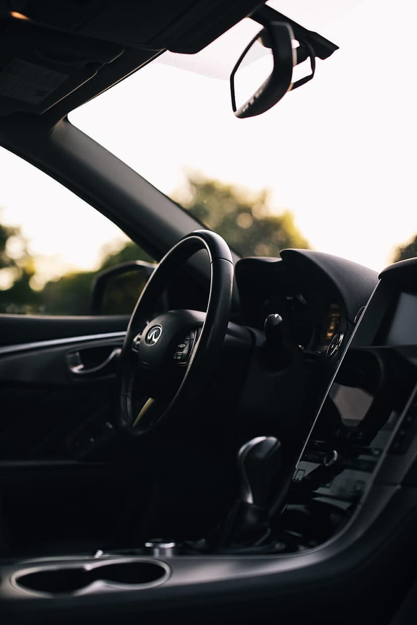 Infiniti steering wheel with a silver logo rests in a modern cabin with a blurred forest background visible.