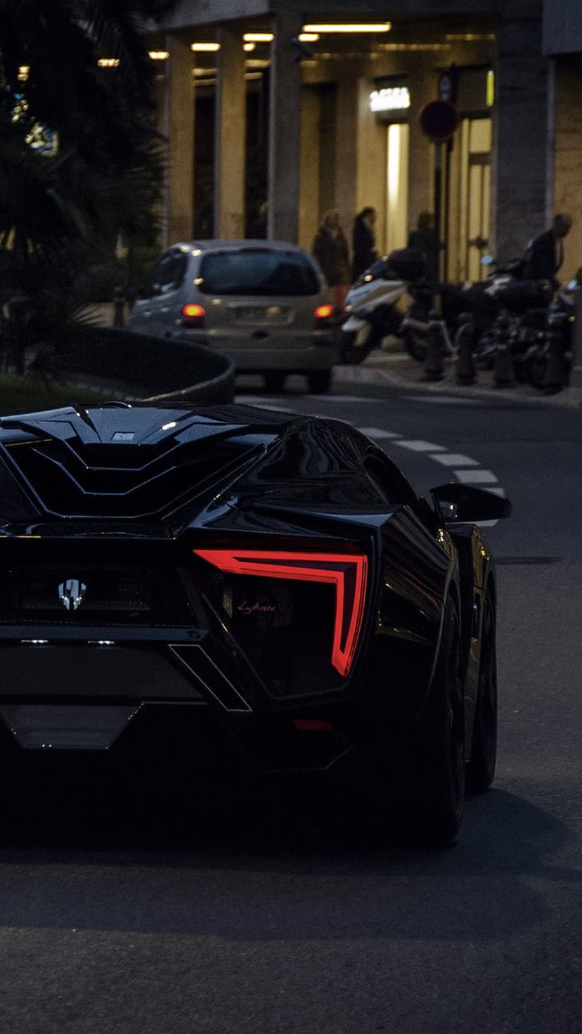 Lykan HyperSport rear view with glowing red L-shaped taillights on a dark urban street during evening twilight.