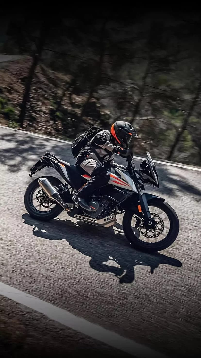 Motorcyclist in full gear leans into a curve on a winding forest road with motion blur on the wheels and pavement.