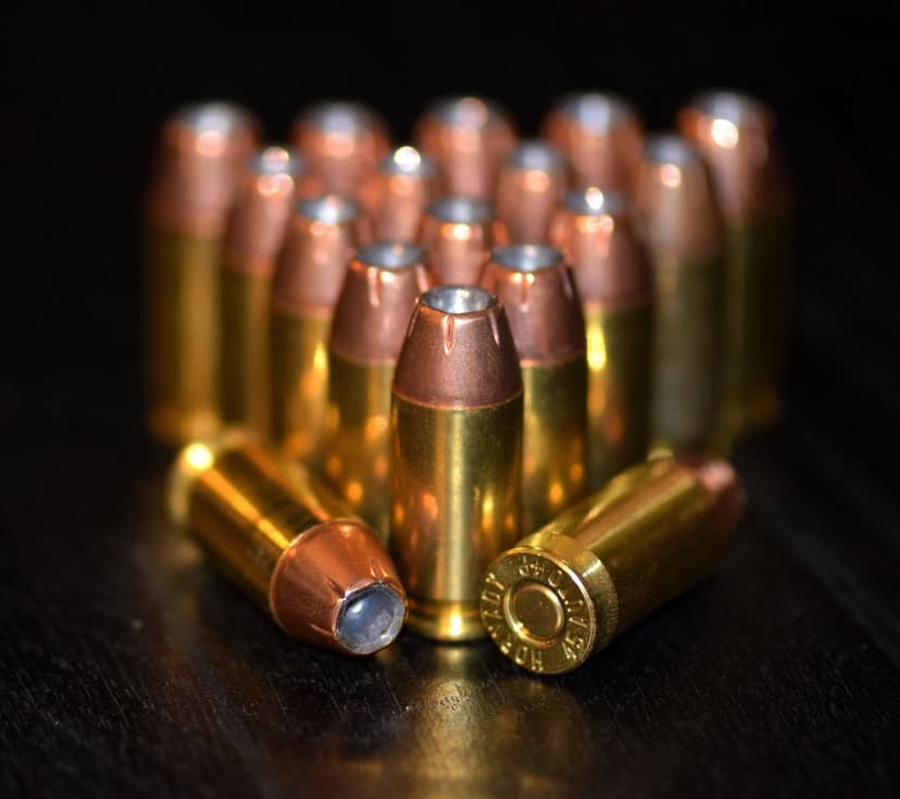 Brass and copper bullets arranged on a dark textured surface with dramatic lighting highlighting metallic details.