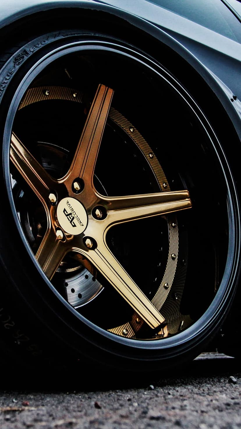 Gold multi-spoke alloy wheel with polished finish and black rubber tire tread on a dark luxury car frame.