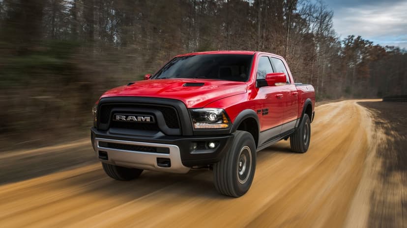 Red Ram 1500 Rebel pickup truck driving fast on a sandy dirt road with motion-blurred trees in the background.