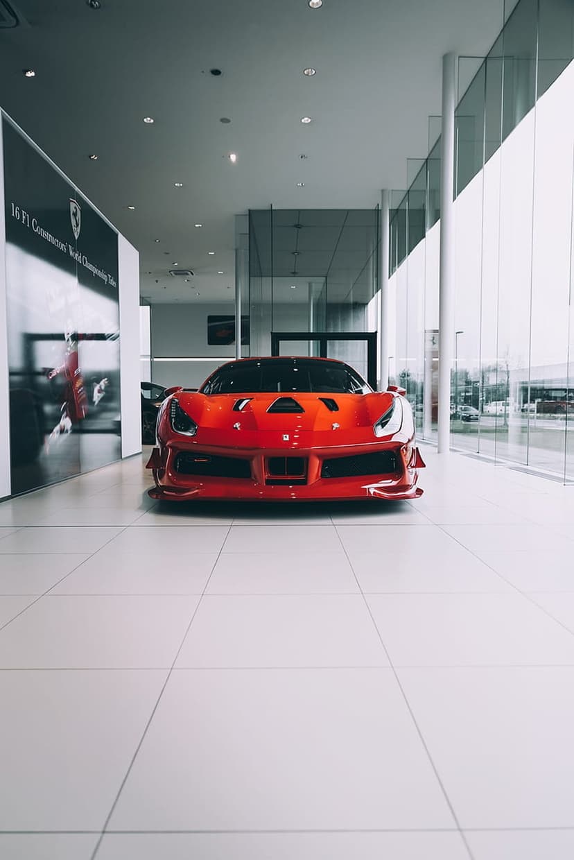 Red Ferrari supercar parked on white tiles inside a glass showroom, showcasing aerodynamic curves and glossy paint.