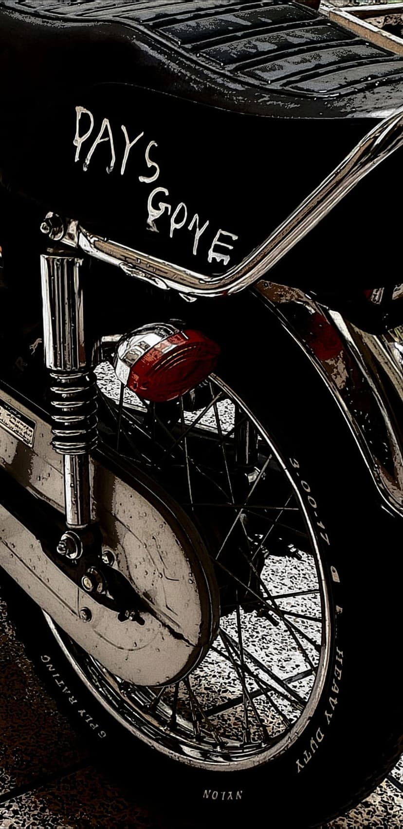 Vintage motorcycle rear wheel and fender featuring white Days Gone text, chrome exhaust, and a red taillight.