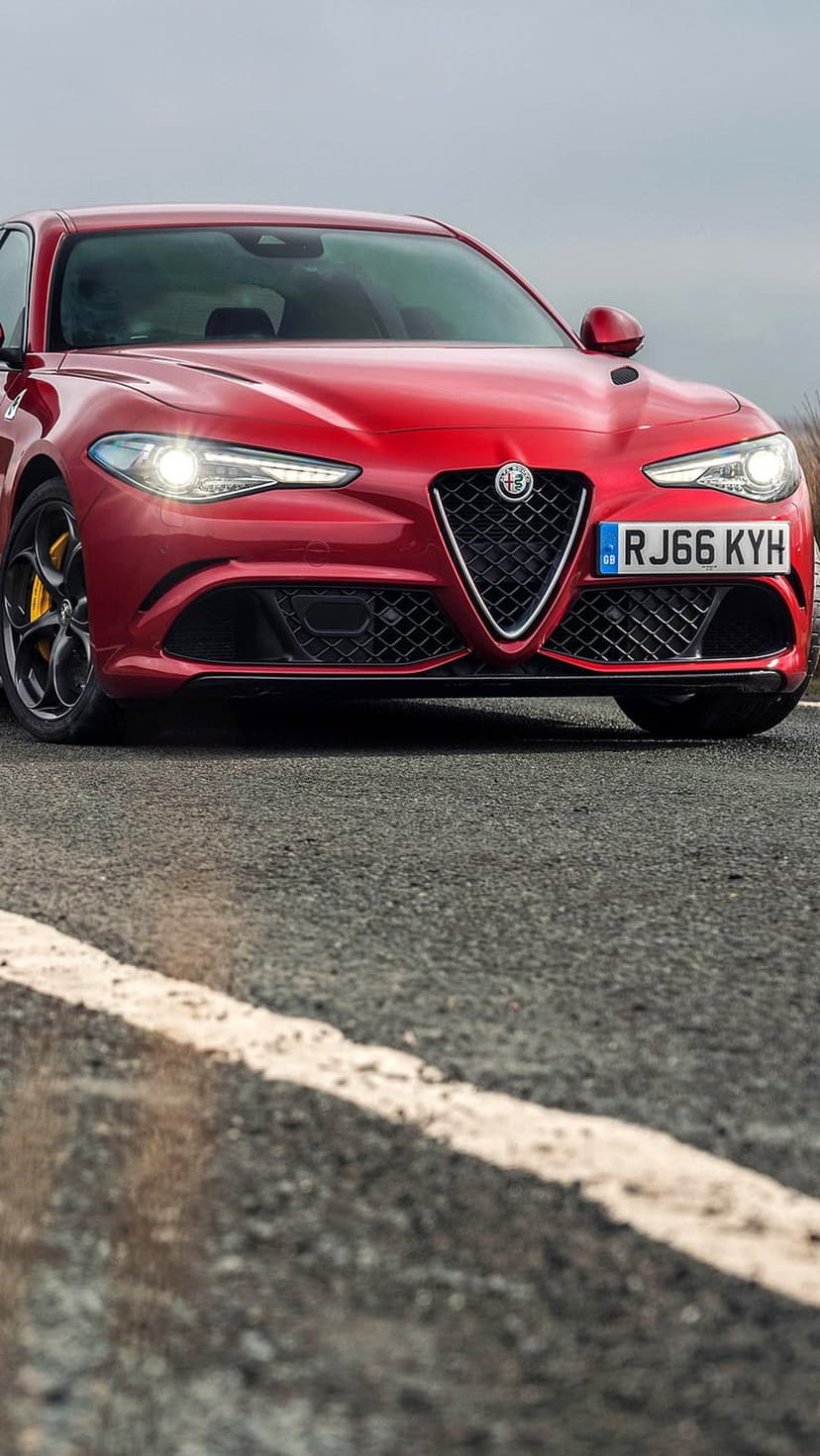 Red Alfa Romeo Giulia Quadrifoglio sports sedan with a signature grille on an asphalt road with white lines.