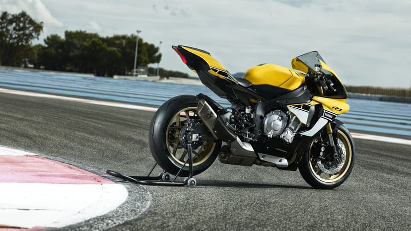 Yellow and black Yamaha YZF-R1 sportbike on a paddock stand at a racetrack under a bright overcast sky.