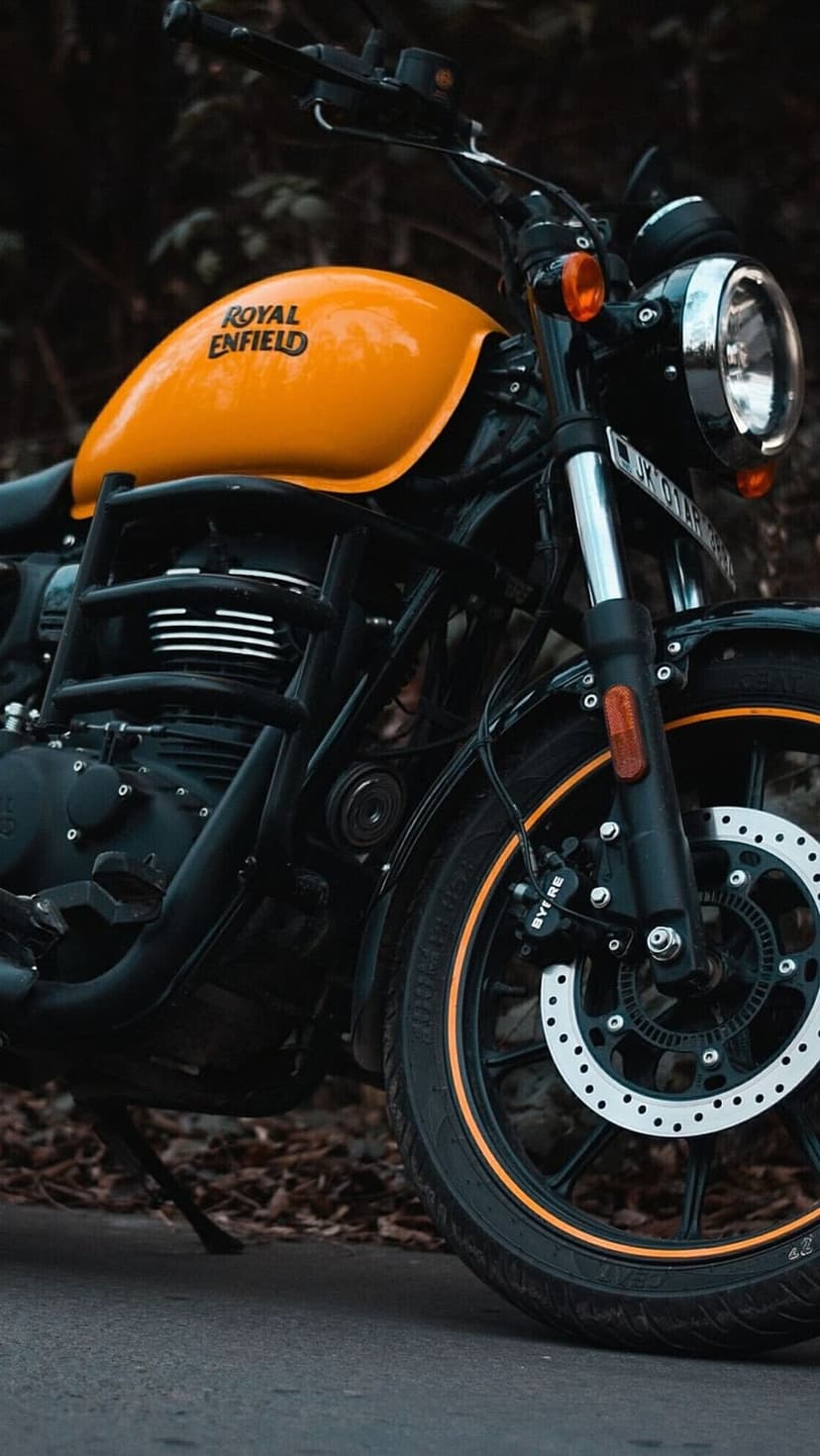 Royal Enfield motorcycle with a bright orange fuel tank, chrome headlight, and black engine in a close-up shot.