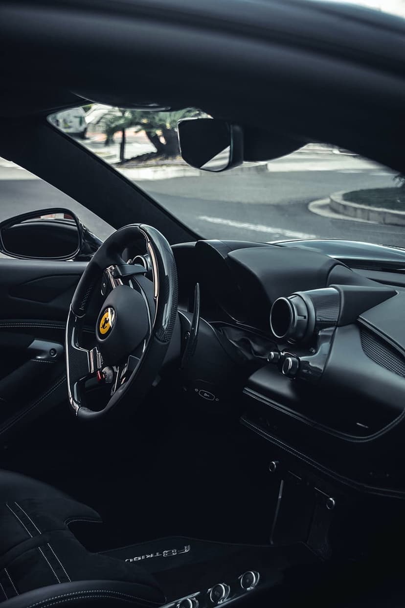 Ferrari steering wheel with yellow emblem and black leather dashboard controls in a luxury supercar cockpit view.