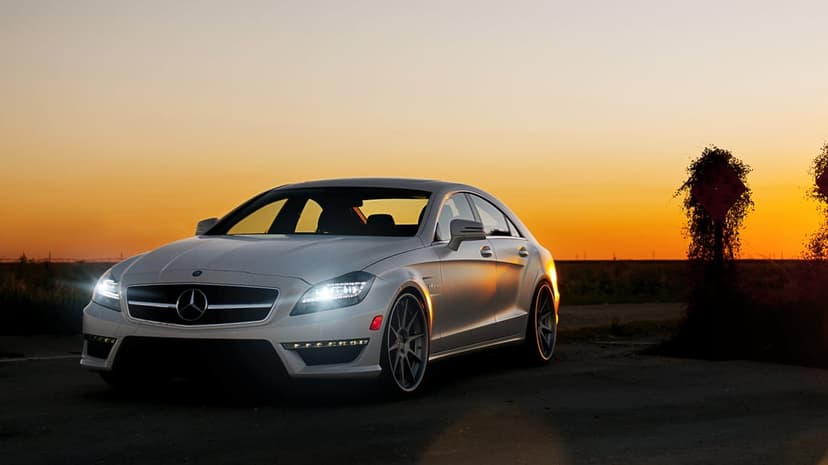 Silver Mercedes-Benz sedan with glowing headlights parked on a rural road during a vibrant orange sunset.