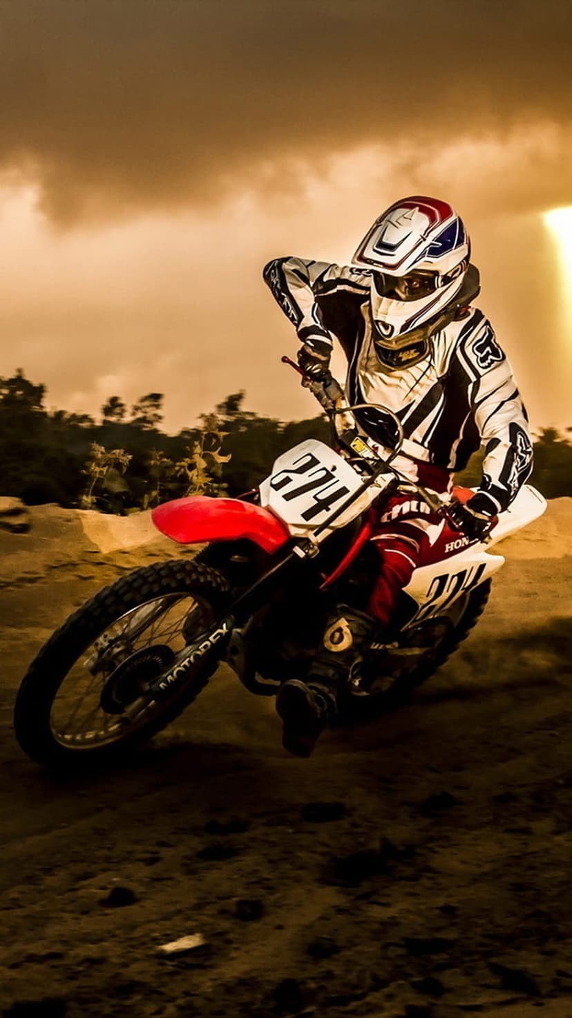 Motocross racer jumping a dirt bike through a hazy golden sunset with clouds of dust kicked up from the track.