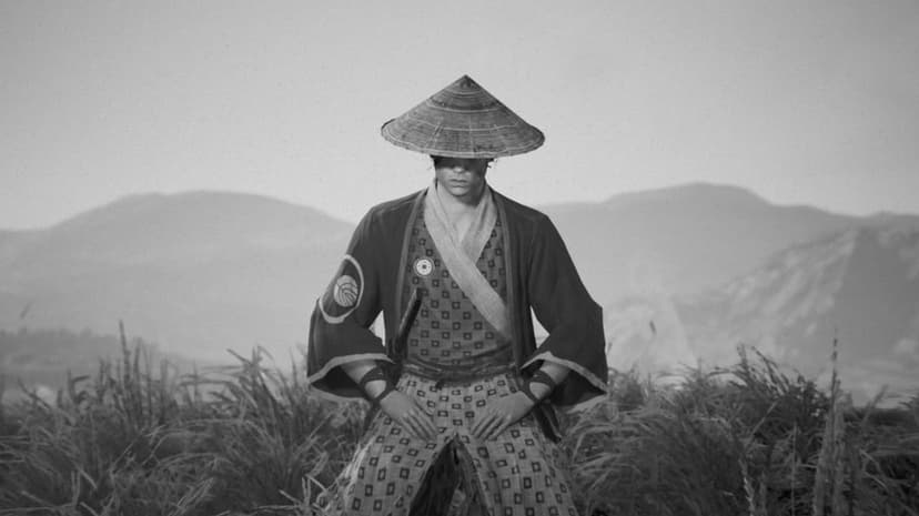 Samurai warrior in a straw hat standing in tall grass with mountains in a black and white landscape.