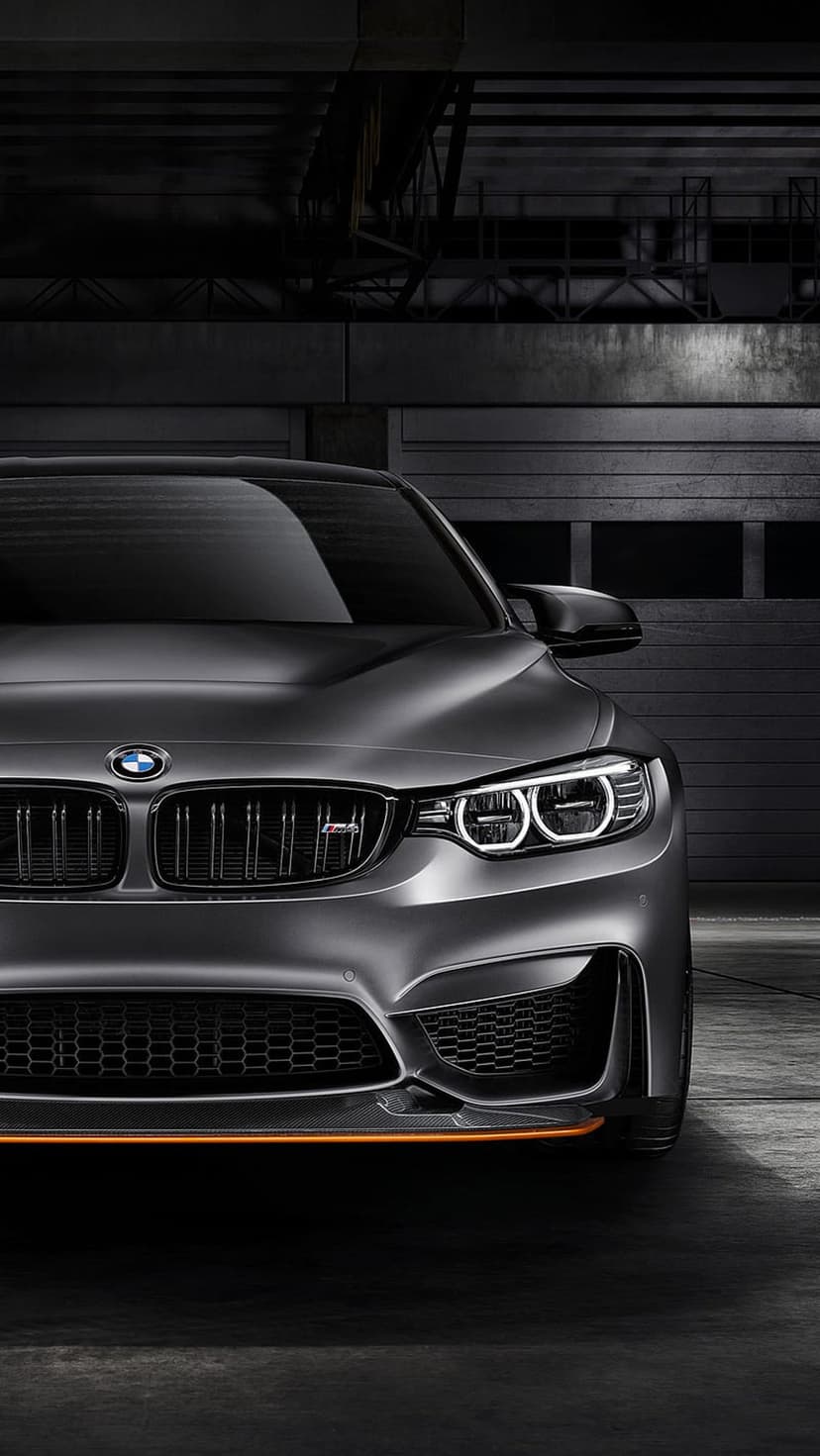 BMW M4 dark gray front grille and LED headlights with orange trim accents in a dim industrial garage setting.