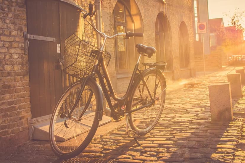 Vintage bicycle with a wicker basket stands on sunlit cobblestones in a quiet European alley during sunset.