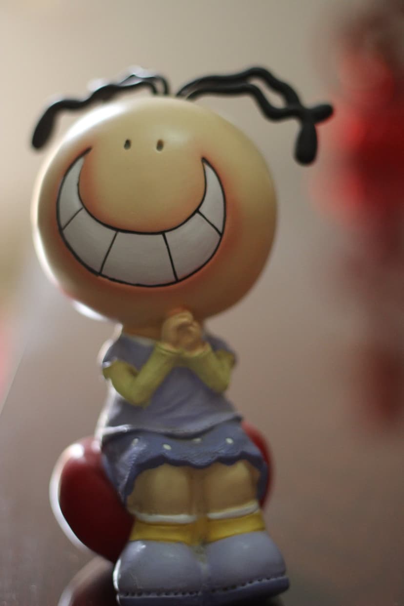 Smiling yellow character in a purple dress sits on a large red heart with a soft blurred background.