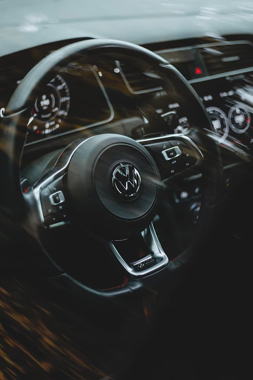 Volkswagen steering wheel with silver logo and integrated controls against a blurred dashboard background.