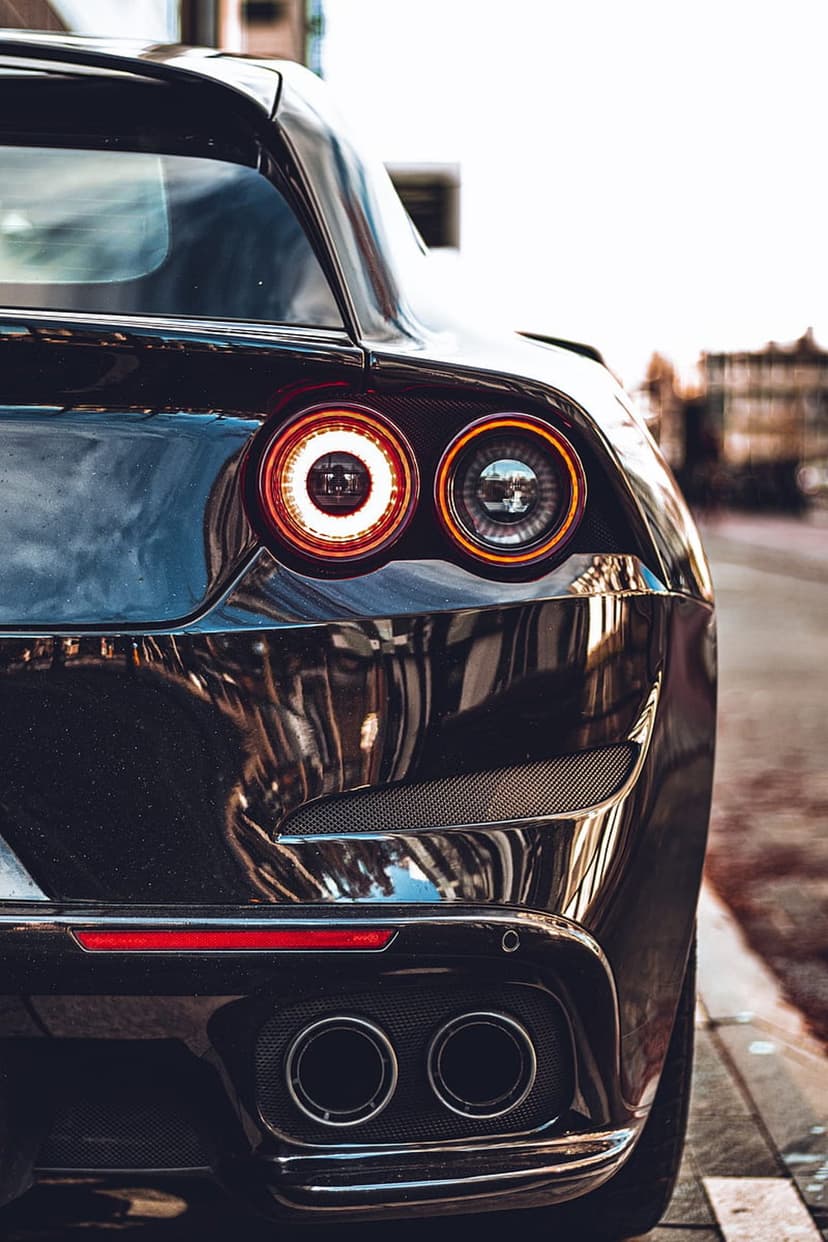 Ferrari circular taillight and dual exhaust pipes on a black car with a textured rear diffuser and reflections.