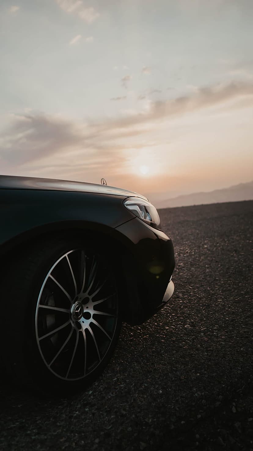 Polished alloy wheel on a gravel desert road reflecting orange sunset light with hazy mountains behind.