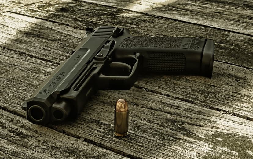 Black handgun resting on a weathered wooden plank next to a single brass bullet in a vertical close-up shot.