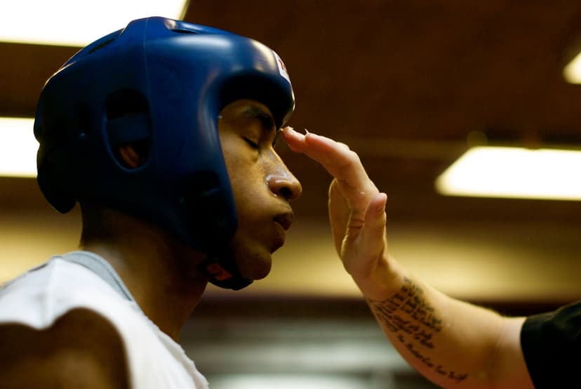 Boxer wearing a blue headguard closes their eyes as a hand rests on their forehead for a pre-match blessing.