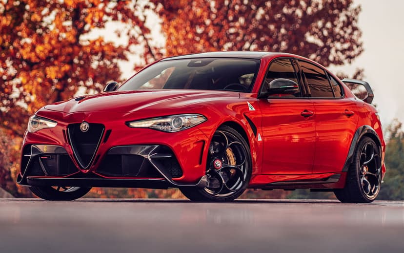 Red Alfa Romeo Giulia GTAm on a road with blurred orange autumn trees and warm golden sunset lighting effects.
