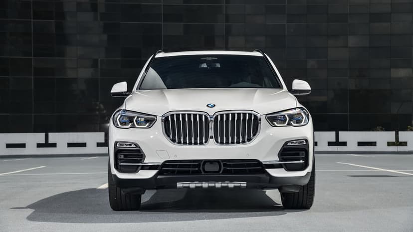 Front view of a white BMW X5 luxury SUV parked on asphalt with a dark textured wall background.