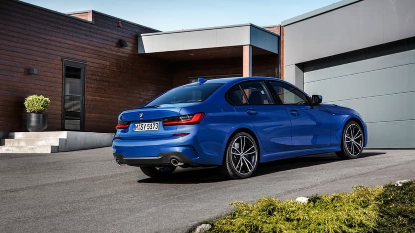Blue BMW 3 Series sedan parked on a driveway in front of a modern house with wood paneling and clear sky.