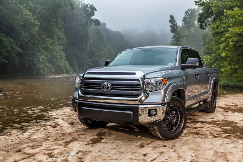 Silver Toyota Tundra pickup truck on a sandy riverbank with a foggy forest and river in the background.
