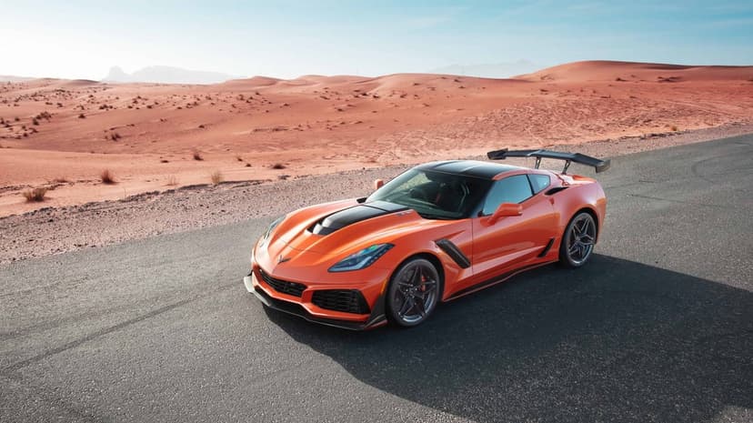 Orange Chevrolet Corvette ZR1 with a large rear wing on a desert road under a clear blue sky.
