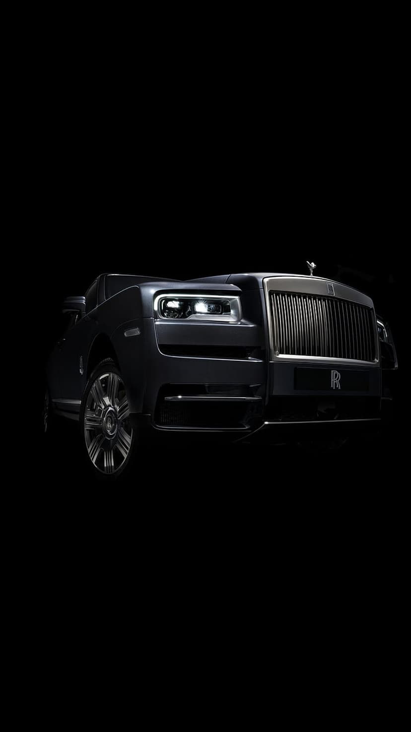 Rolls-Royce Cullinan SUV front grille and Spirit of Ecstasy ornament illuminated against a dark black background.