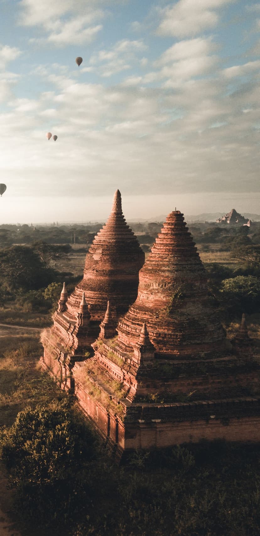 Hot air balloons floating over ancient stone pagodas in Bagan during a misty golden sunrise in Myanmar.