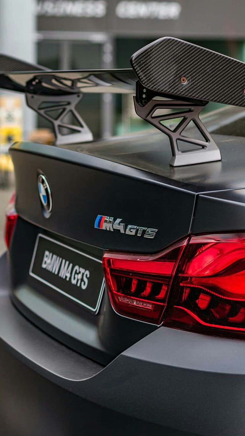 BMW M4 GTS rear showcases a matte black exterior, carbon fiber spoiler wing, and sharp red LED taillights.