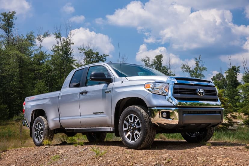 Silver Toyota Tundra TRD 4x4 pickup truck on a dirt mound against a bright blue sky with fluffy white clouds.