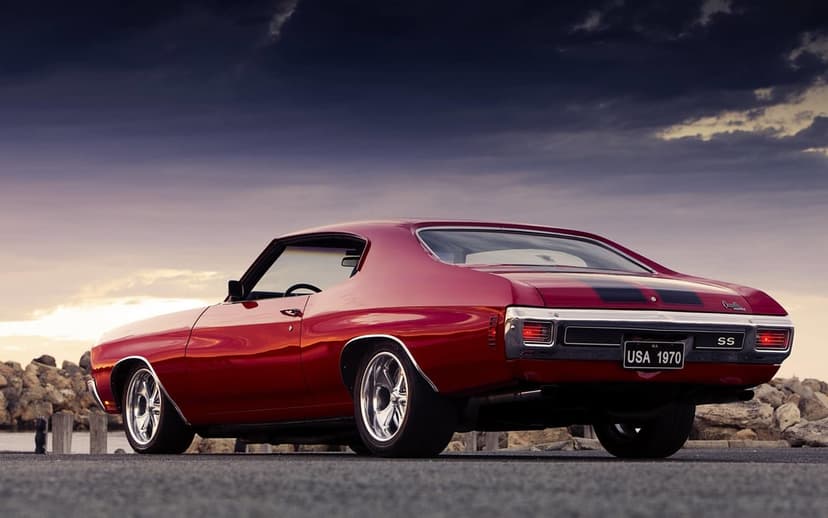 Red 1970 Chevy Chevelle SS parked on asphalt under a dark stormy sky with a golden horizon at sunset.