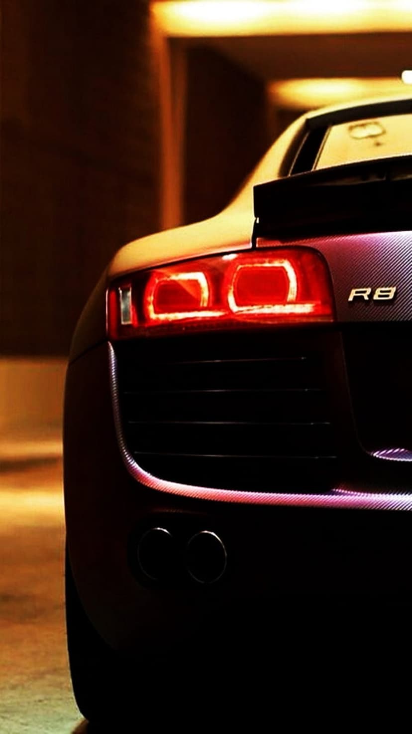 Audi R8 rear tail lights and dual exhausts illuminate a dark night scene with a red glowing aesthetic.