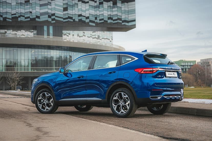 Metallic blue Haval F7 SUV parked on an asphalt road in front of a modern geometric glass building.